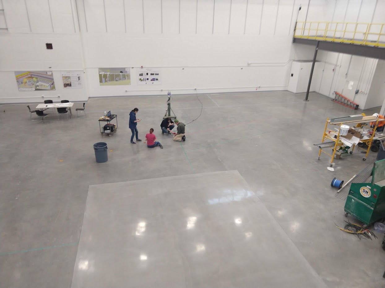 overhead shot of a large, empty experimental hall with a few people surveying the floor below