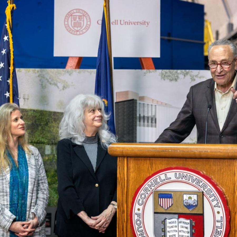 Image of three women watching Sen. Schumer address from a podium. Description in caption.