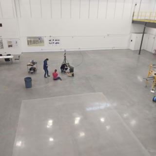 overhead shot of a large, empty experimental hall with a few people surveying the floor below